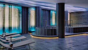 Un área interior de piscina moderna con sillones de descanso, una zona de estar circular y paneles de luz verticales.