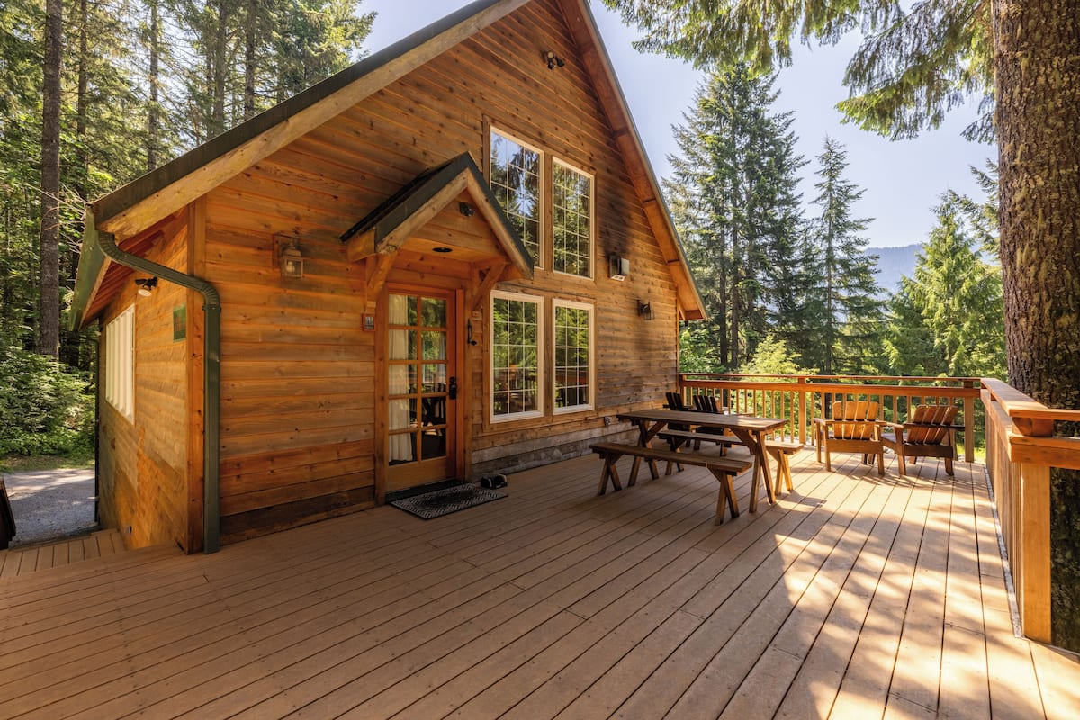 A wooden cabin with a deck, large windows, and a door.
