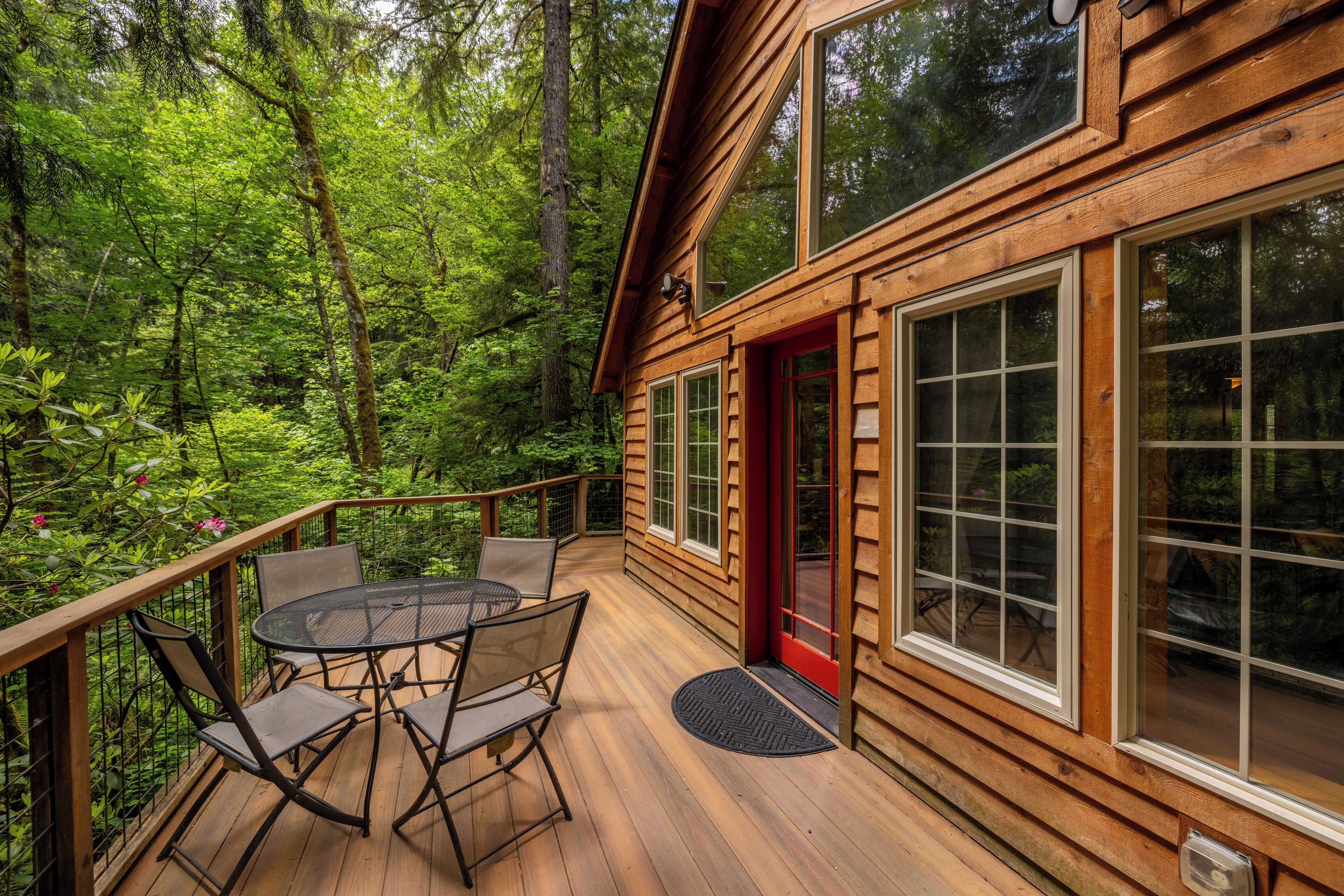 A wooden deck with a table and chairs, surrounded by a forest.