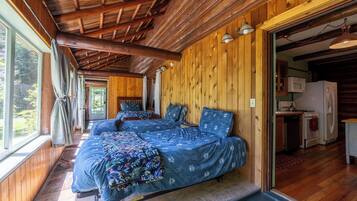 A cabin with two beds, wooden walls, a kitchen area, and large windows.