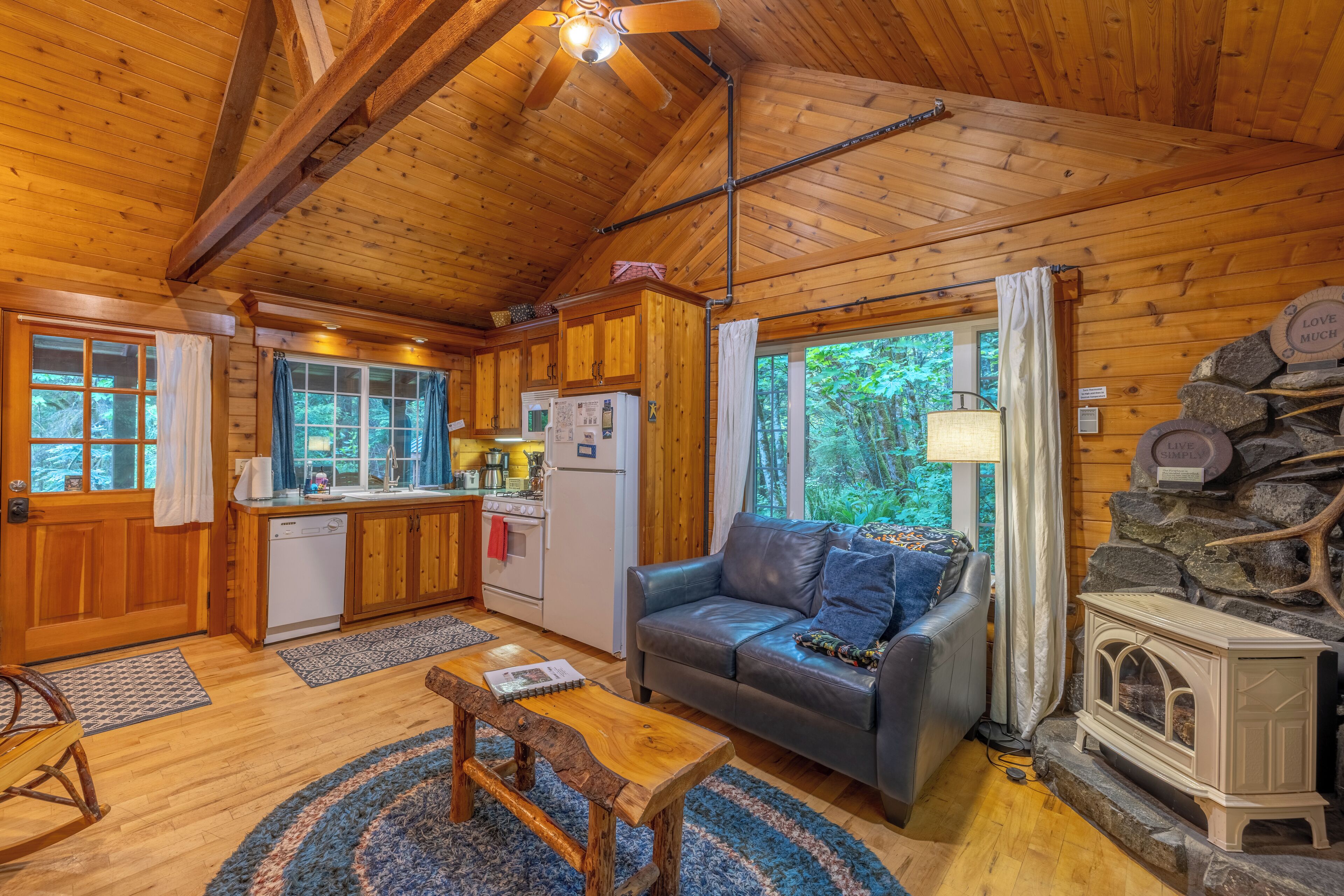 A cozy cabin interior with wooden walls, a kitchen, a living area with a sofa, and a stone fireplace.