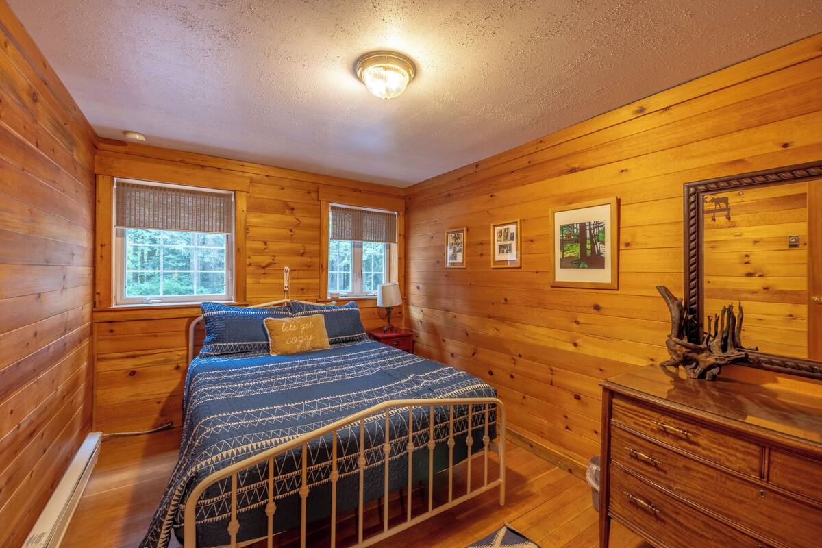 A wooden-paneled bedroom with a bed, dresser, and framed pictures on the wall.