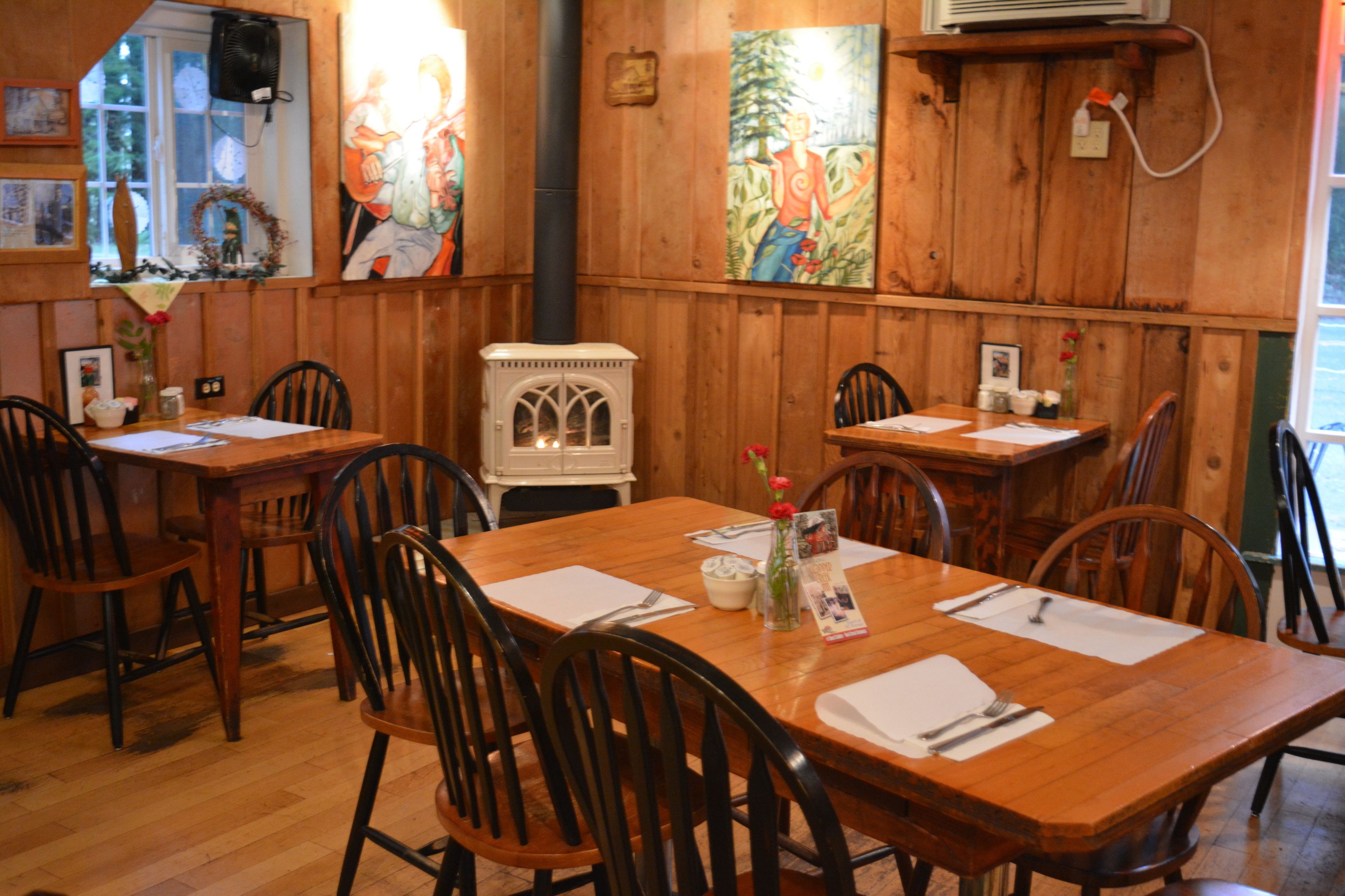 A wooden interior with tables and chairs, a white stove, and artwork on the walls.