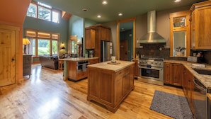 A spacious kitchen with wooden cabinets, a large island, and a stainless steel range hood. - Copper Creek Inn at Mt Rainier (Ashford)