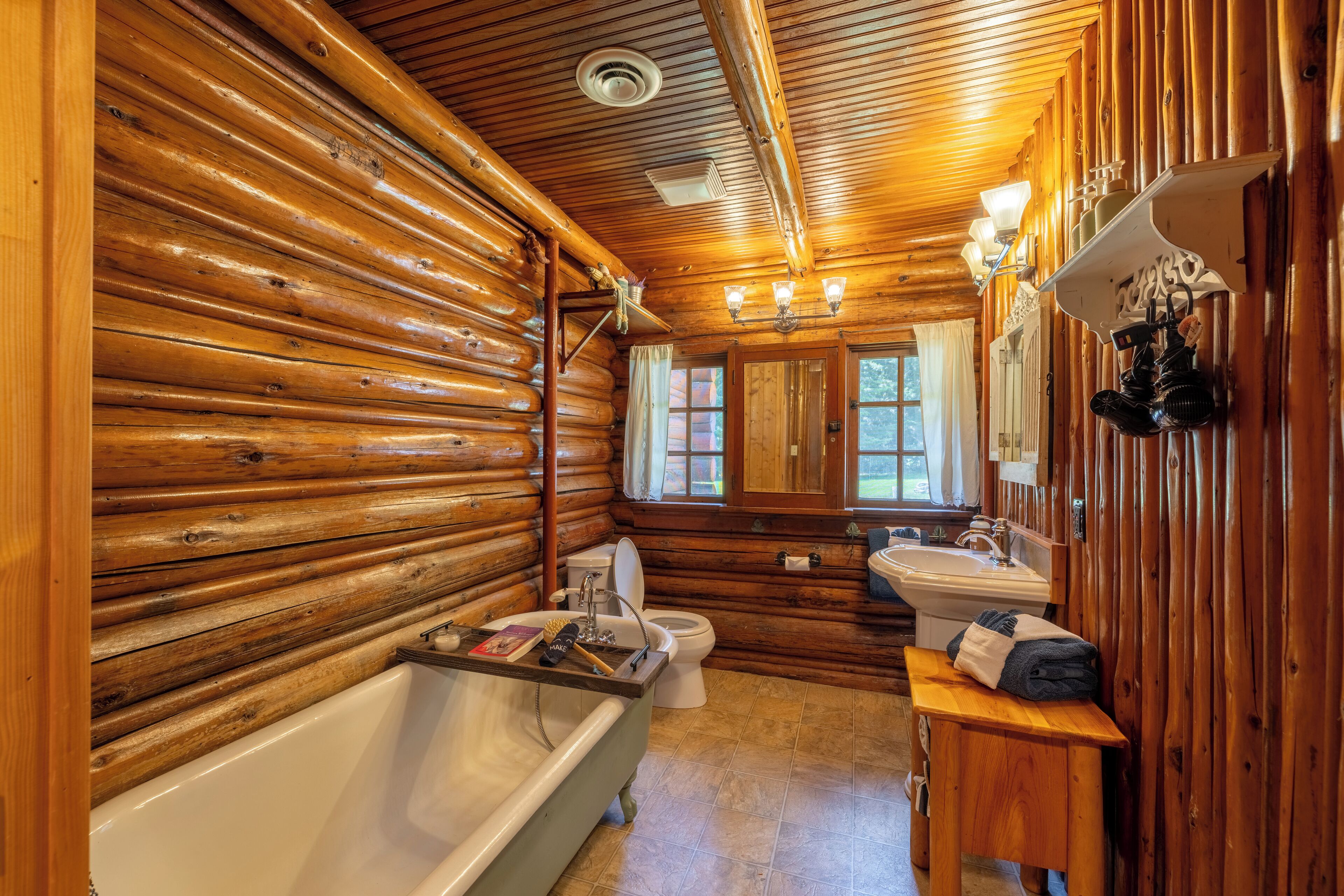 A log cabin bathroom with a bathtub, toilet, sink, and wooden walls.