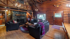 A log cabin interior with a stone fireplace, wooden floors, and a high ceiling. - Copper Creek Inn at Mt Rainier (Ashford)