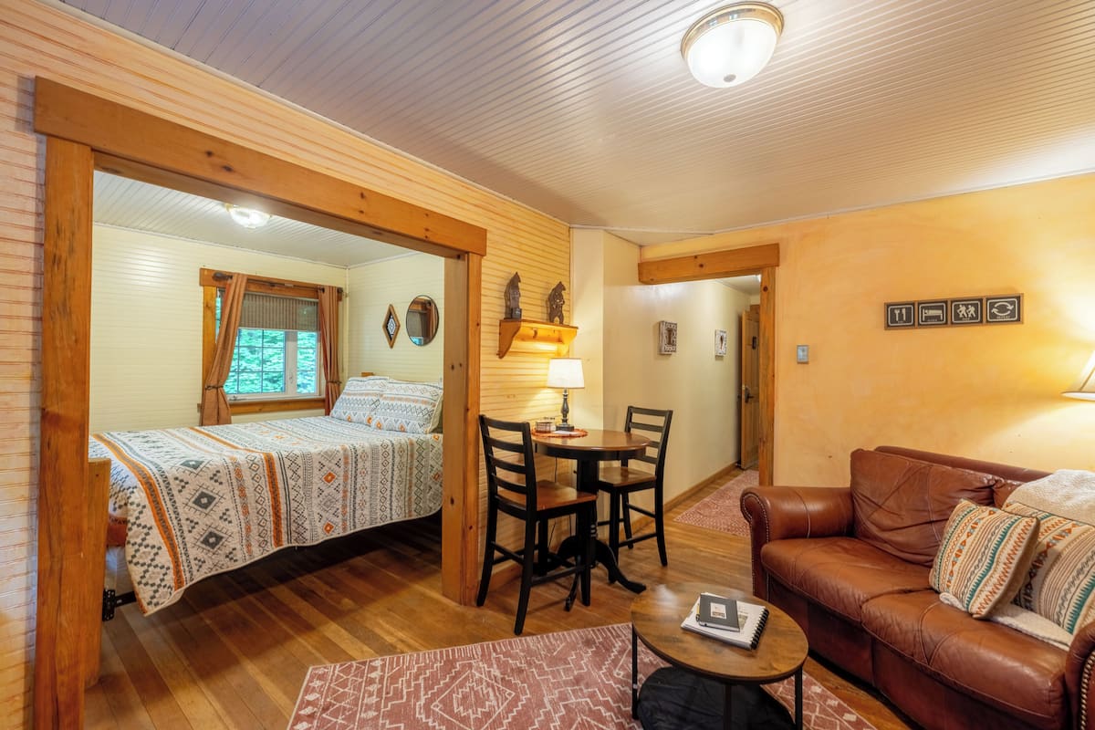 A cozy room with a bed, a brown leather couch, a small table, and a chair.