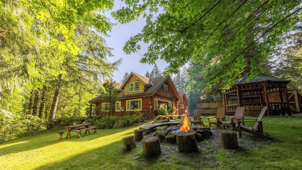 A cabin with a fire pit surrounded by wooden stumps, a picnic table, and a wooden deck. - Copper Creek Inn at Mt Rainier (Ashford)