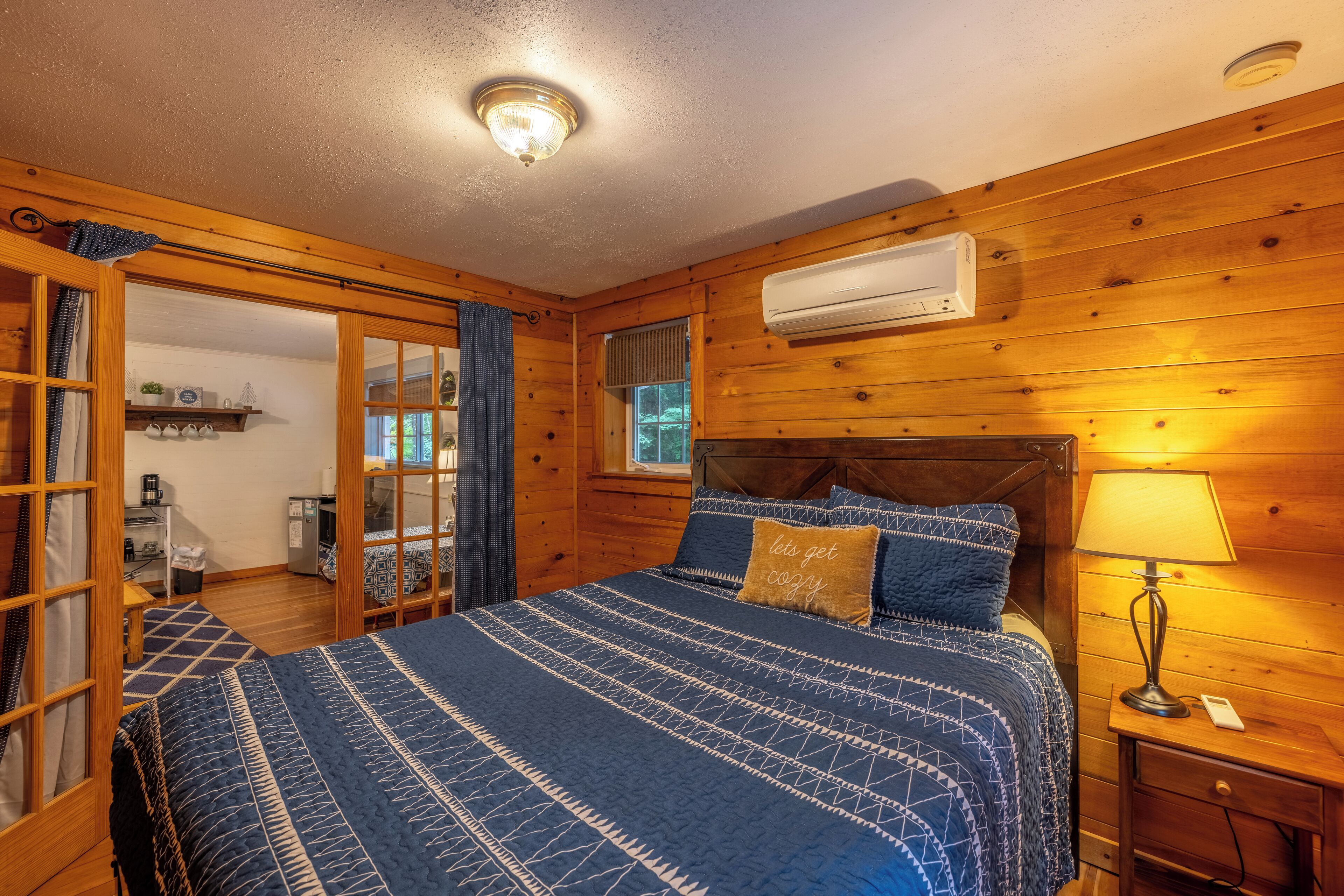Une chambre dans un chalet en bois, comprenant un lit, une table de chevet, un appareil de climatisation et une fenêtre.