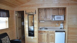 Ein gemütliches Holzhaus mit Küchenzeile, einem Spiegel, einem schwarzen Ledersessel und einem Bett.