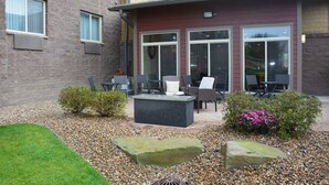 Ein Außenbereich mit Terrasse, einem Steinkamin, Sitzmöglichkeiten und einem kleinen Garten mit Steinen und Sträuchern.