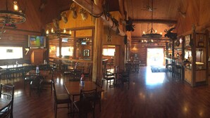 A spacious restaurant with wooden interiors, multiple tables and chairs, and a variety of mounted animal heads on the walls.