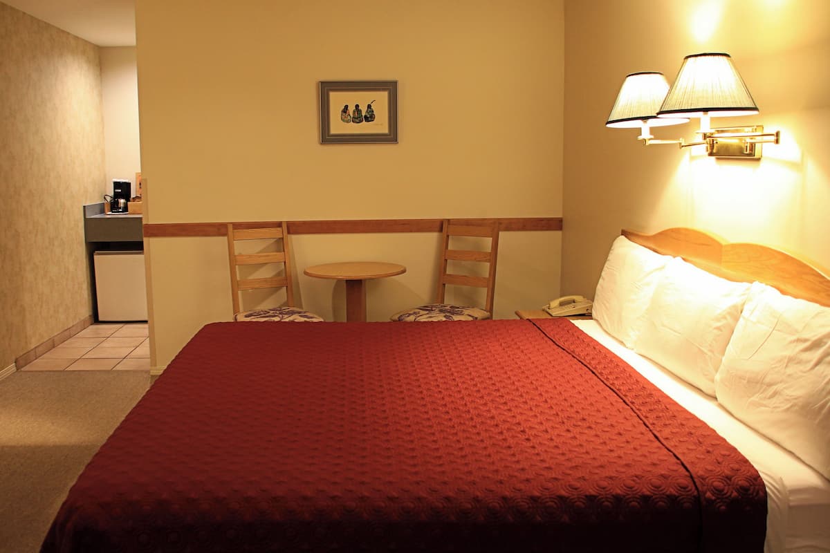 Quarto de hotel com uma cama grande, uma mesinha, duas cadeiras, uma escrivaninha com cafeteira e um telefone.