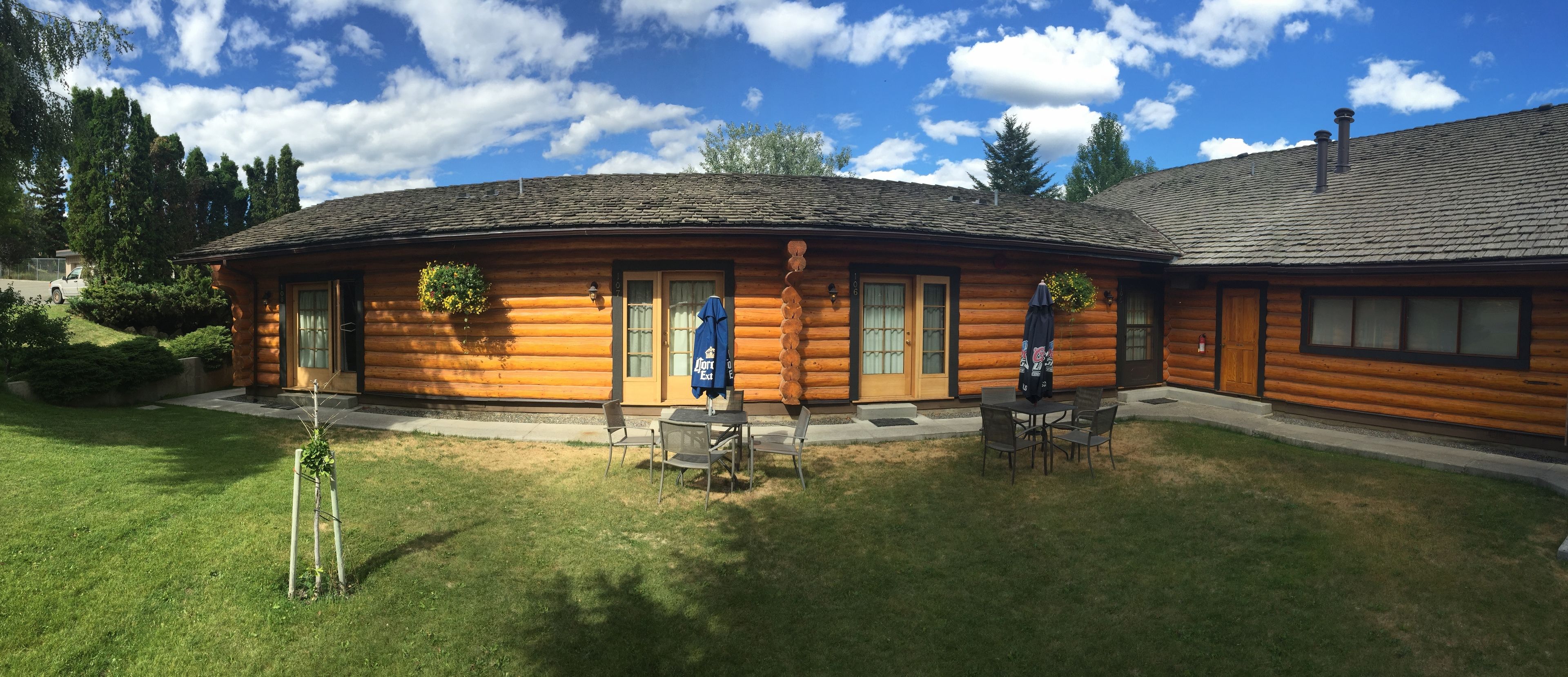 A log cabin with a covered patio, outdoor seating, and a well-maintained lawn.