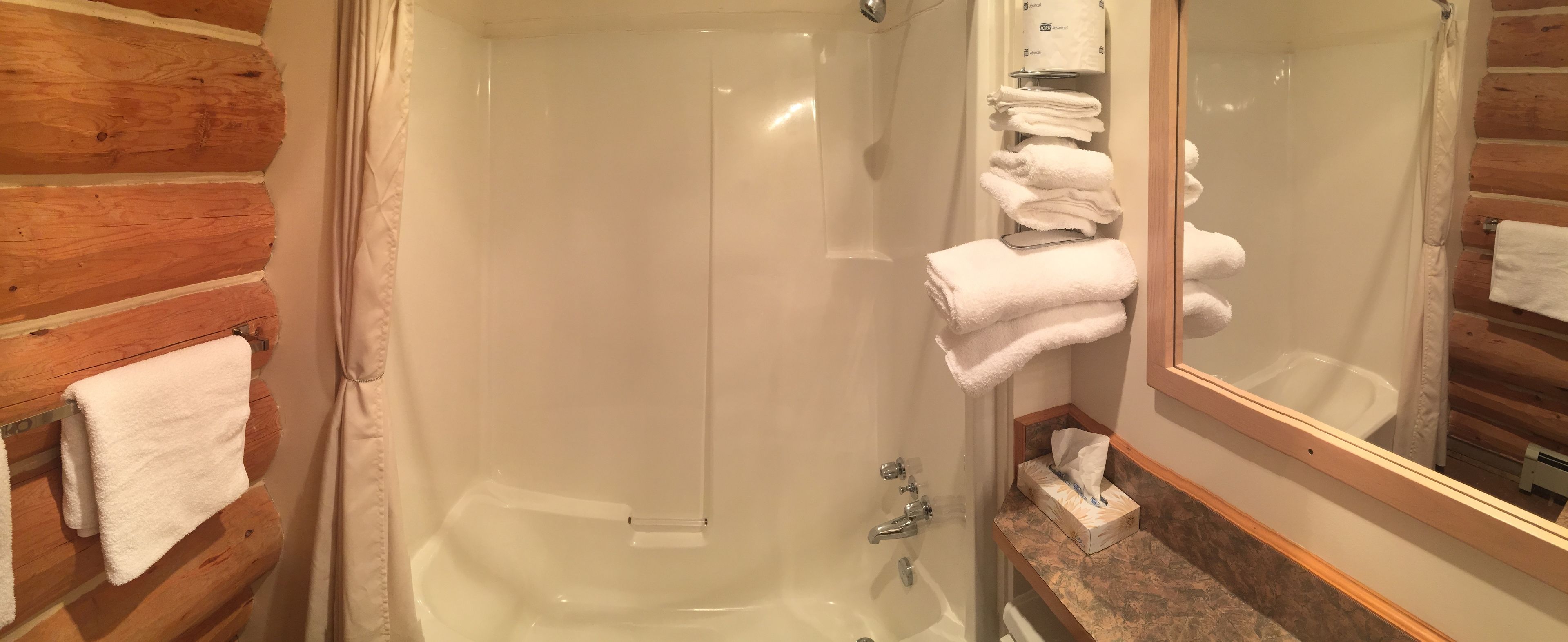 Une salle de bain avec un mur en bois, une baignoire, un miroir et un porte-serviettes.