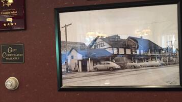 A black and white photo of a historic hotel with a prominent sign, a vintage car parked in front, and a smaller building in the background.