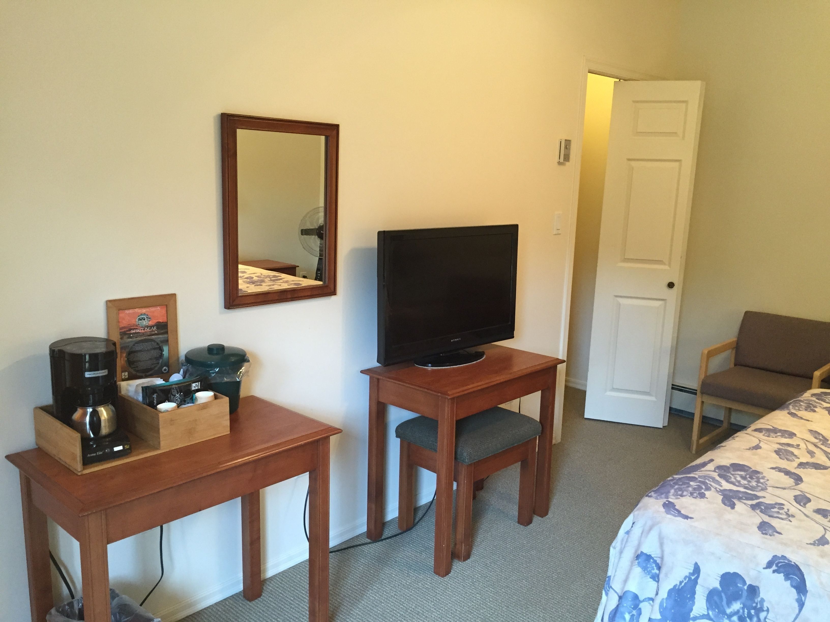 A hotel room with a wooden desk, a television, a chair, and a bed with a floral bedspread.
