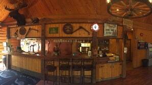 A rustic bar area with wooden walls, a counter, and a sign for 'The Cariboo Lodge'.
