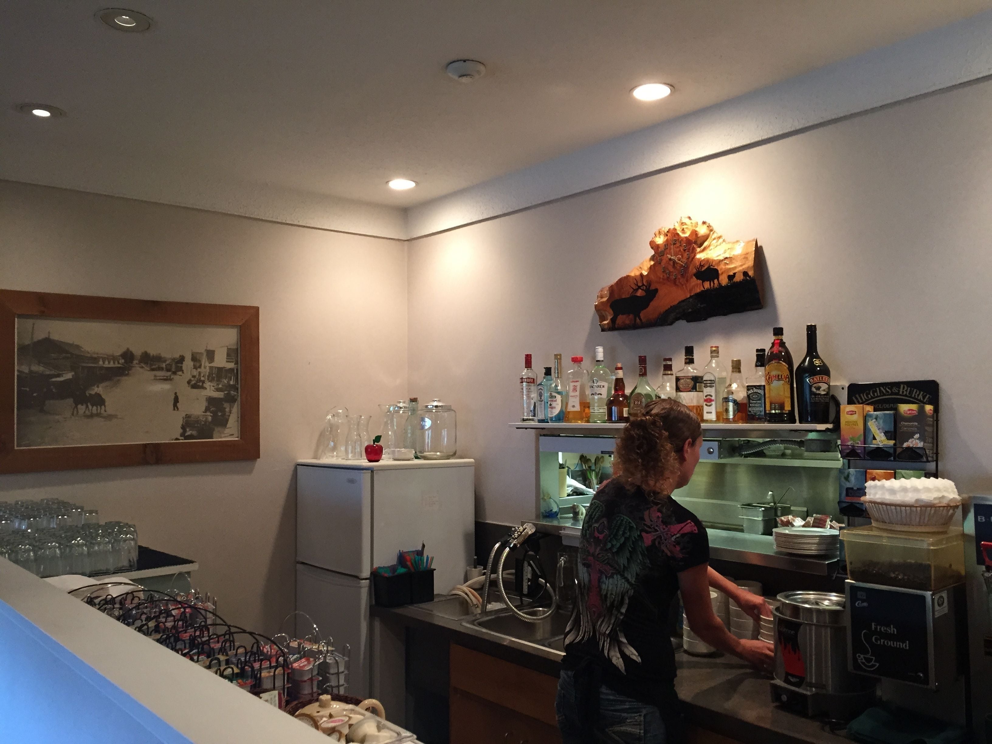 Un coin bar équipé d’un réfrigérateur, de bouteilles, de verres et orné d’un tableau au mur.
