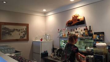 Un coin bar équipé d’un réfrigérateur, de bouteilles, de verres et orné d’un tableau au mur.