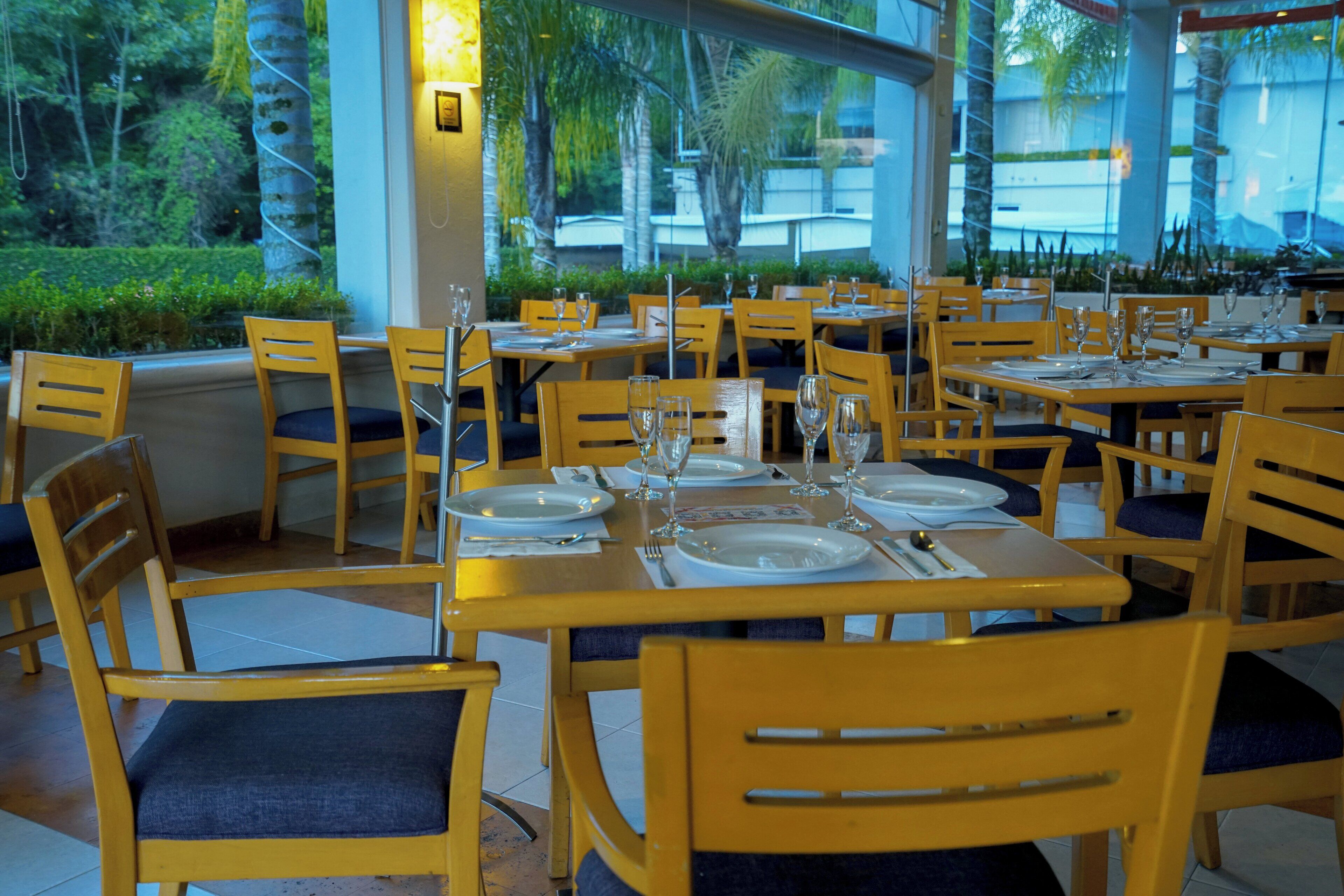 A restaurant with wooden tables and chairs, set for dining with plates, glasses, and cutlery.
