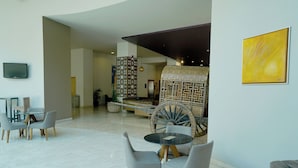 A modern lobby with a large wooden wagon wheel centerpiece, grey upholstered chairs, and a flat-screen TV mounted on the wall. - Gamma by Fiesta Americana Xalapa Nubara (Xalapa)