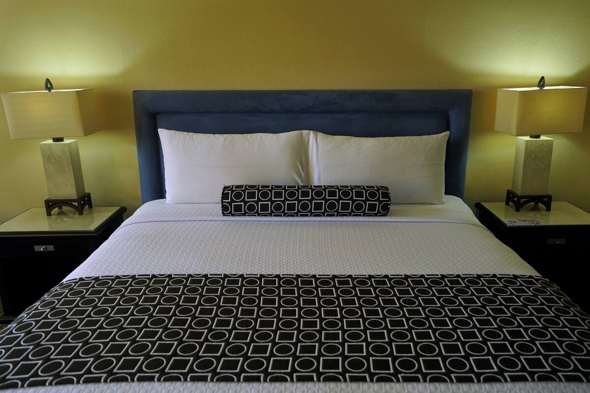 A neatly made bed with a patterned bedspread, a blue headboard, and two bedside lamps.