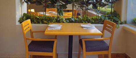 A dining area with a wooden table and two chairs, surrounded by potted plants.