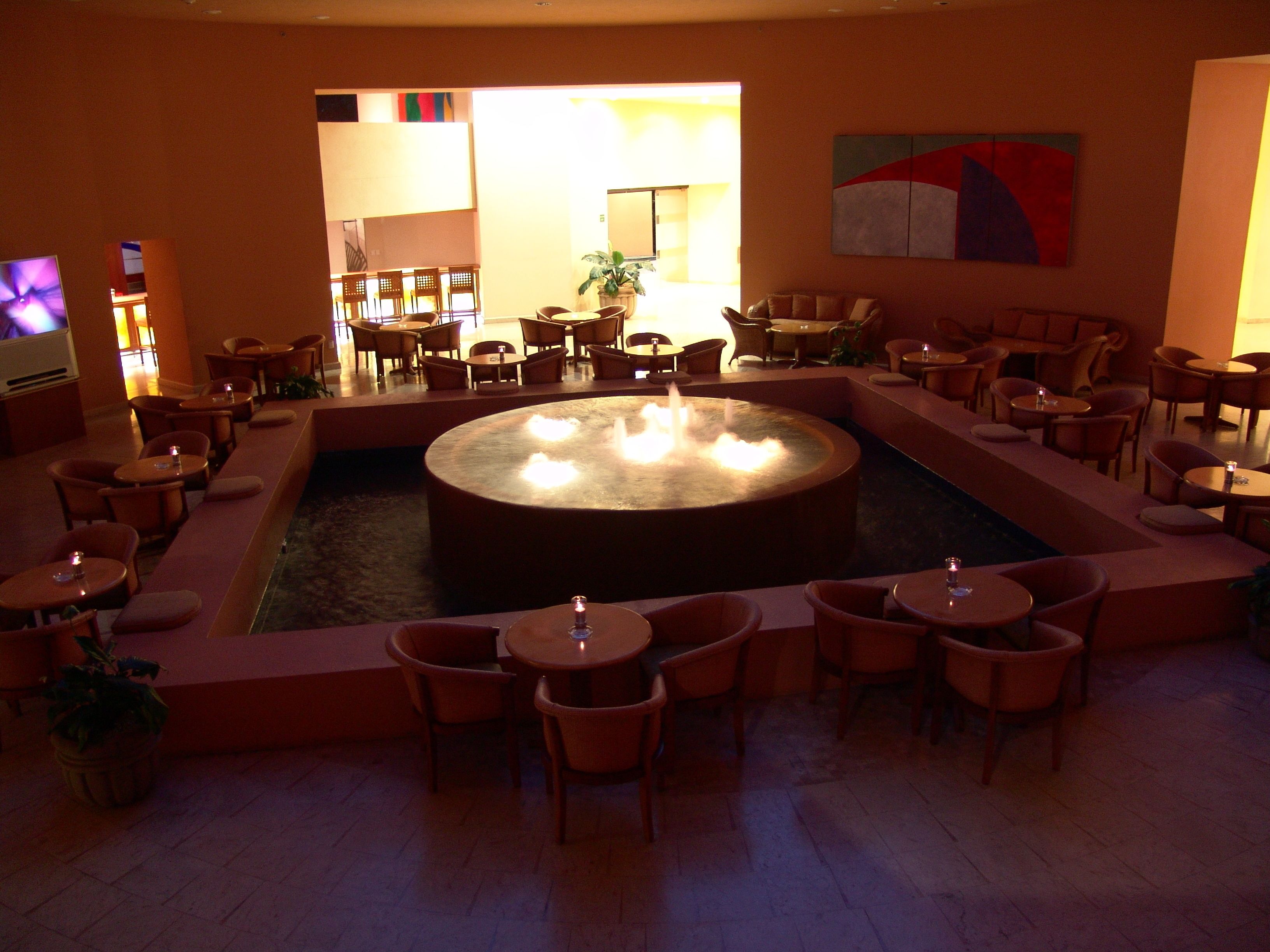 Un área de estar con una mesa circular central, diferentes disposiciones de asientos y una pequeña fuente de agua.