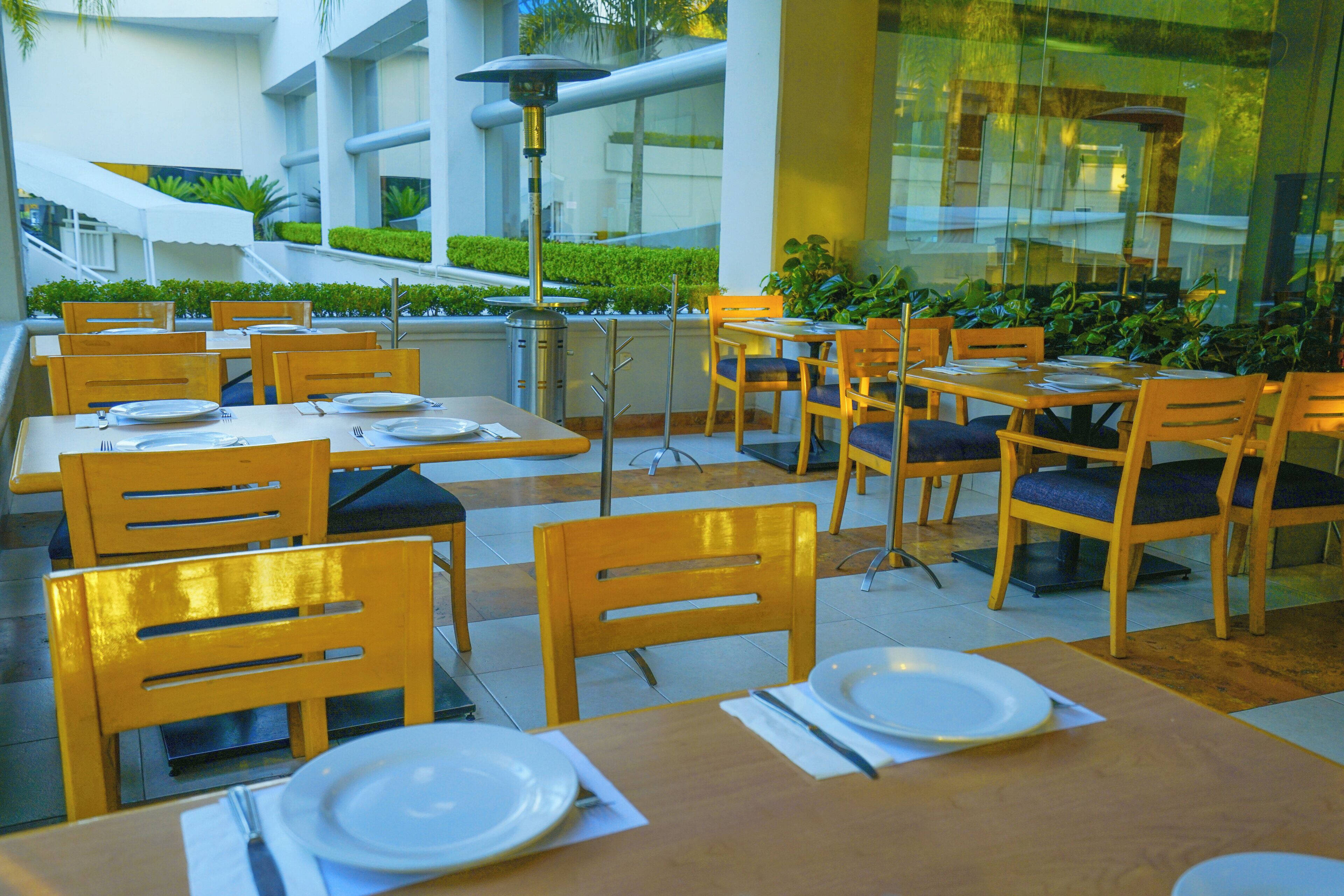 A restaurant with multiple tables and chairs, some with blue cushions.