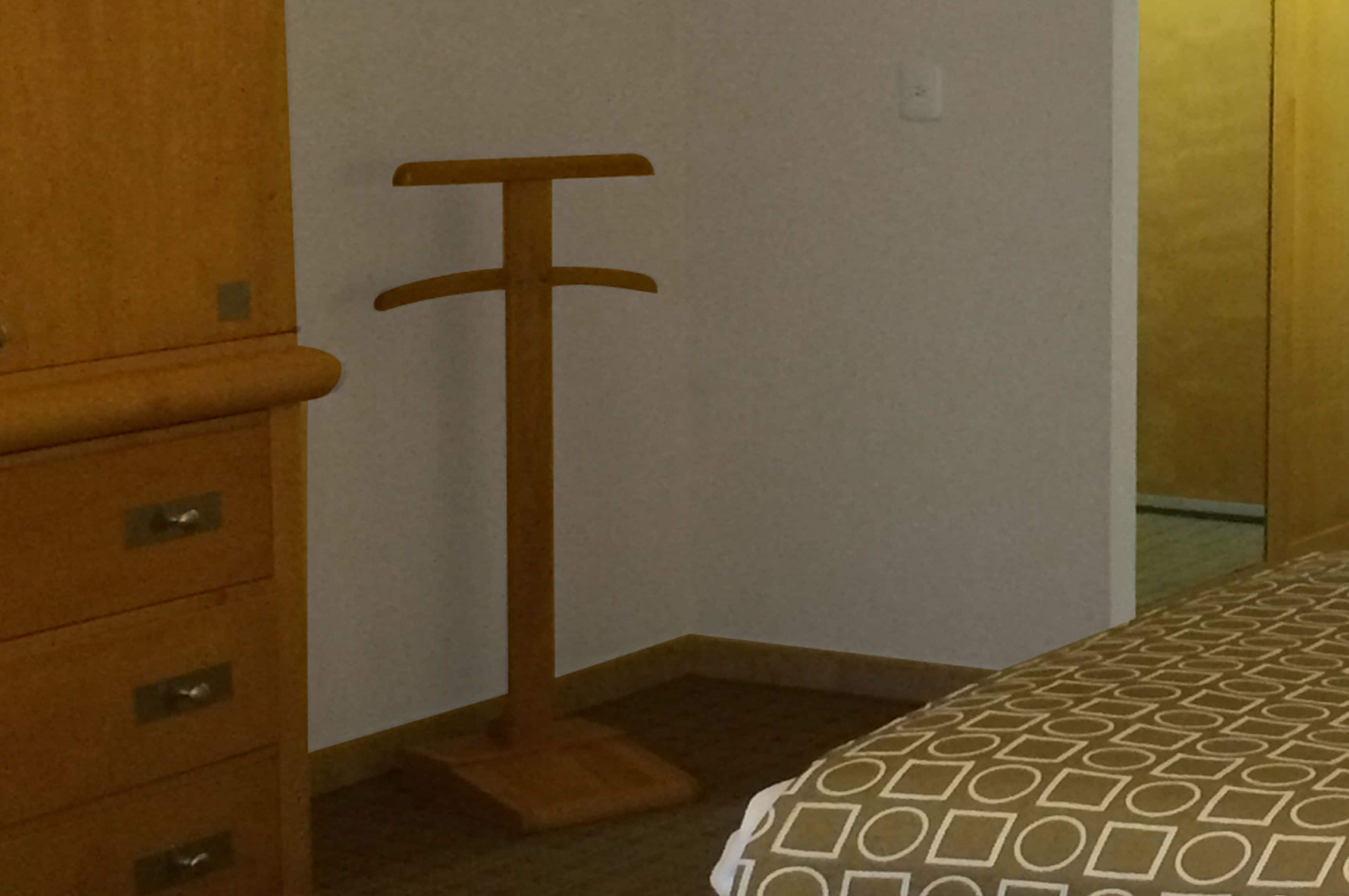 Un rincón de una habitación con un aparador de madera, un perchero y una cama con colcha estampada.
