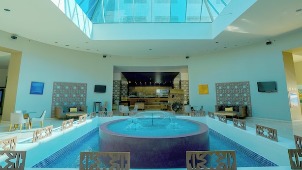 A spacious lobby with a central pool, a reception desk, and a high ceiling with skylights. - Gamma by Fiesta Americana Xalapa Nubara (Xalapa)