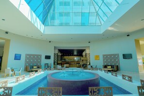 A spacious lobby with a central pool, a reception desk, and a high ceiling with skylights. - Gamma by Fiesta Americana Xalapa Nubara (Xalapa)