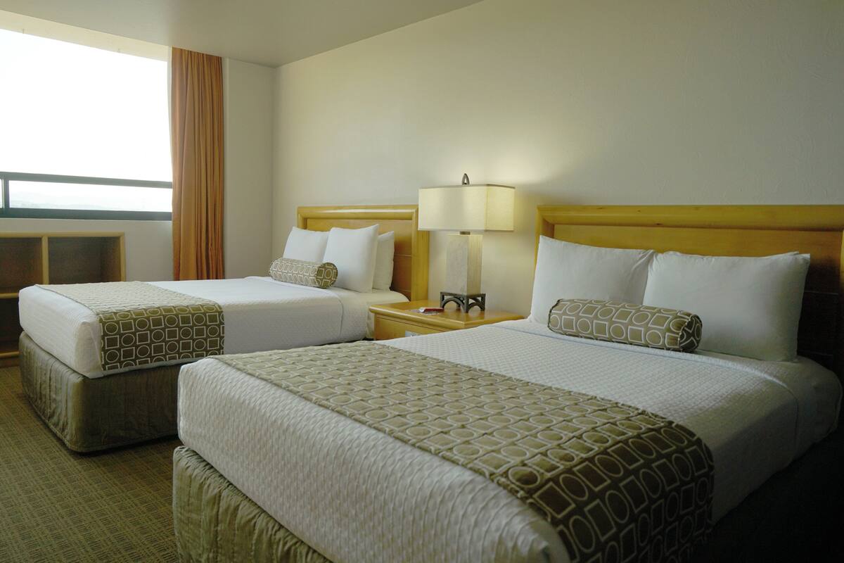 A hotel room with two beds, a nightstand with a lamp, and a window with curtains.