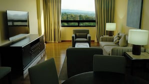A hotel room with a flat-screen TV, a sofa, a chair, a dining table, and a view of the outdoors through large windows. - Gamma by Fiesta Americana Xalapa Nubara (Xalapa)