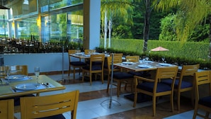 A restaurant with wooden tables and chairs, a glass wall, and a view of greenery. - Gamma by Fiesta Americana Xalapa Nubara (Xalapa)