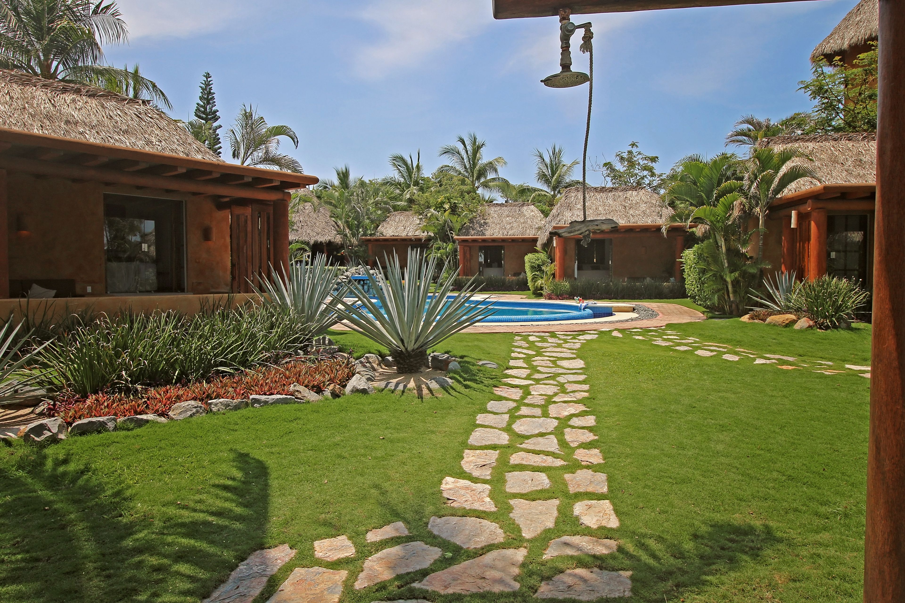 A resort with thatched-roof cottages, a swimming pool, and a stone pathway.