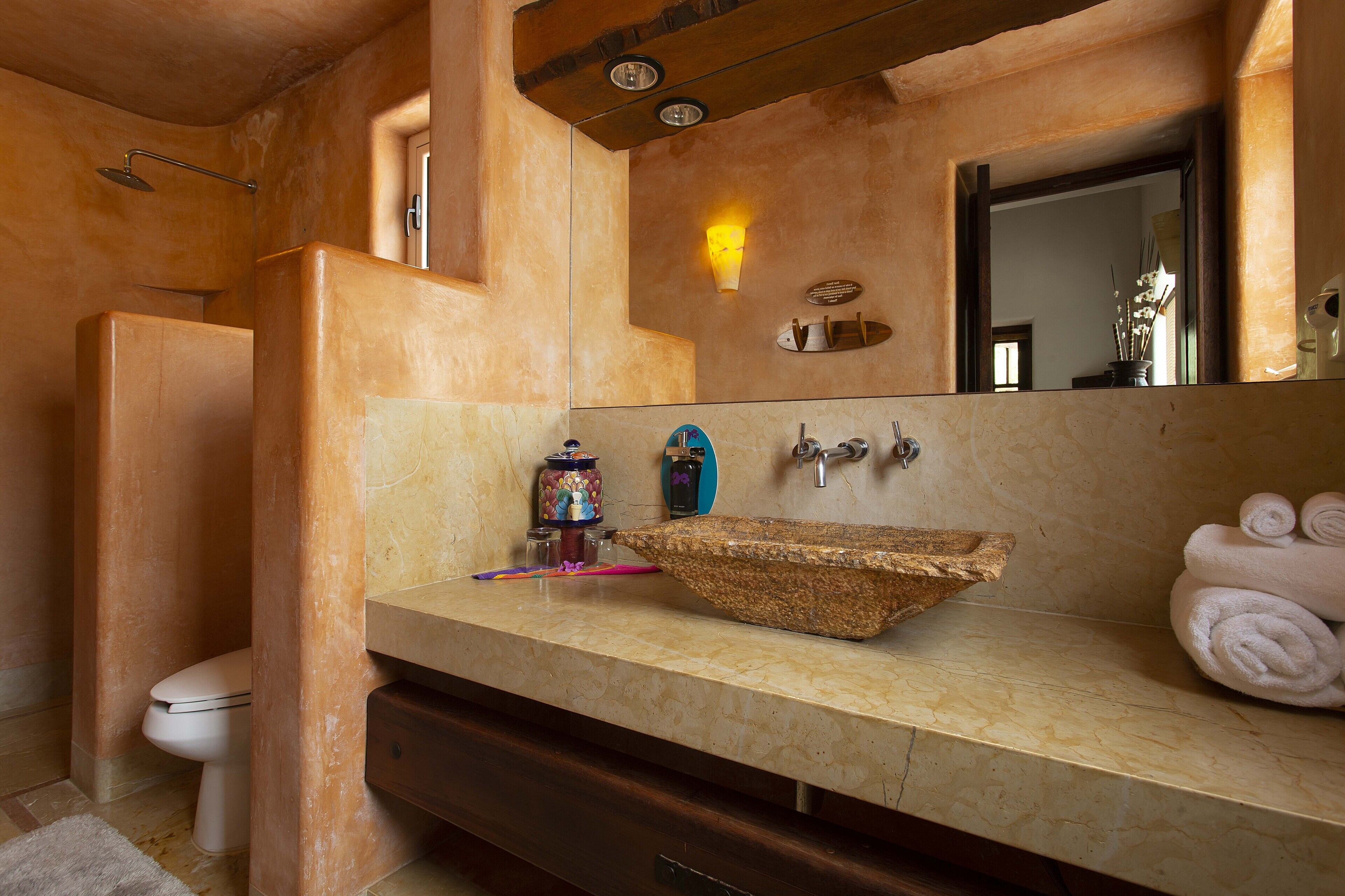 Un baño con un lavamanos grande y rústico, un inodoro y una ducha.