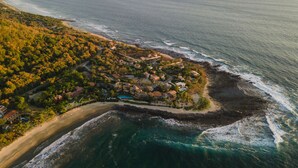 An aerial view of a coastal resort with multiple buildings, a beach, and a rocky shoreline.