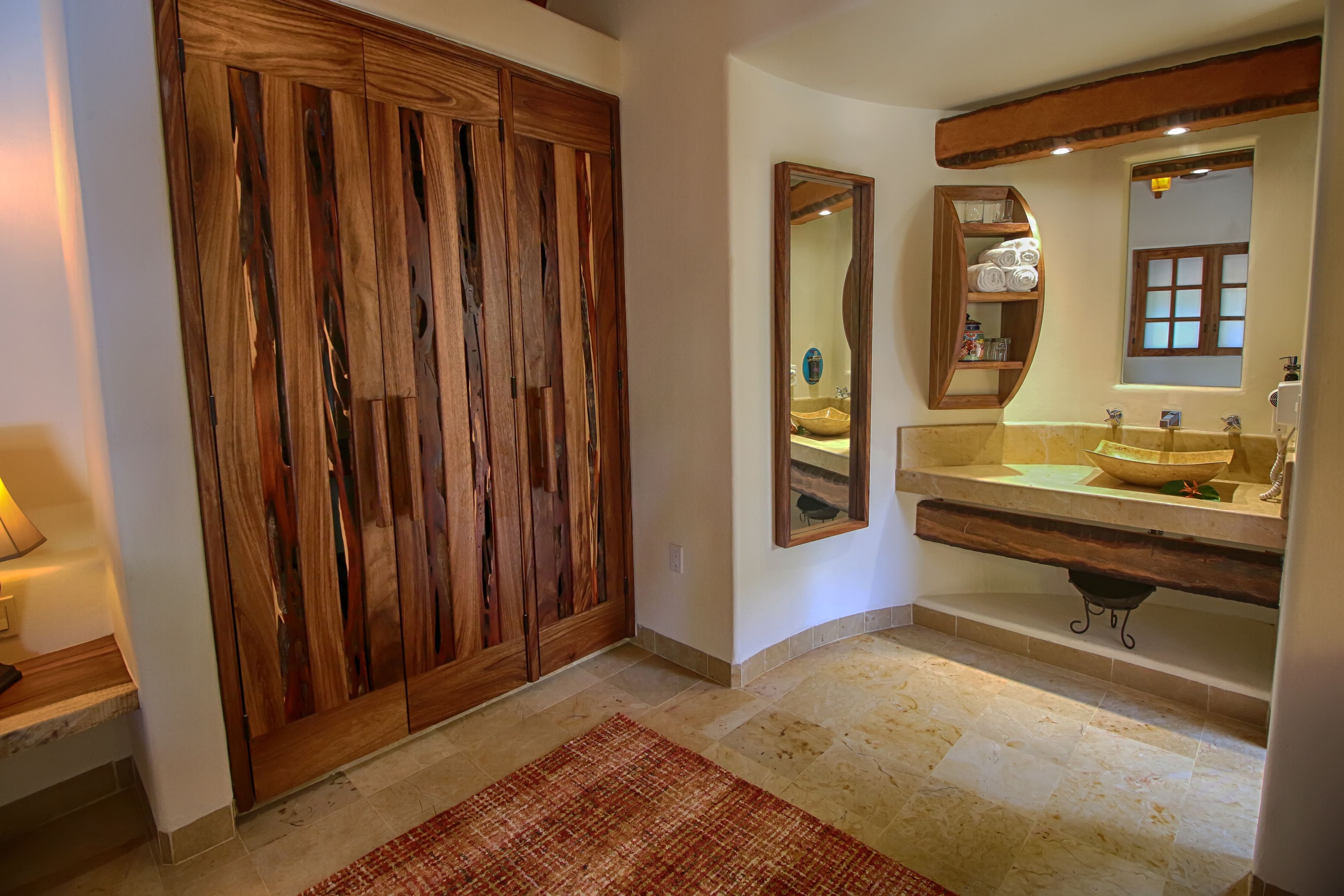 Un baño con un armario de madera, un espejo grande, un lavabo y una ventana con vistas.