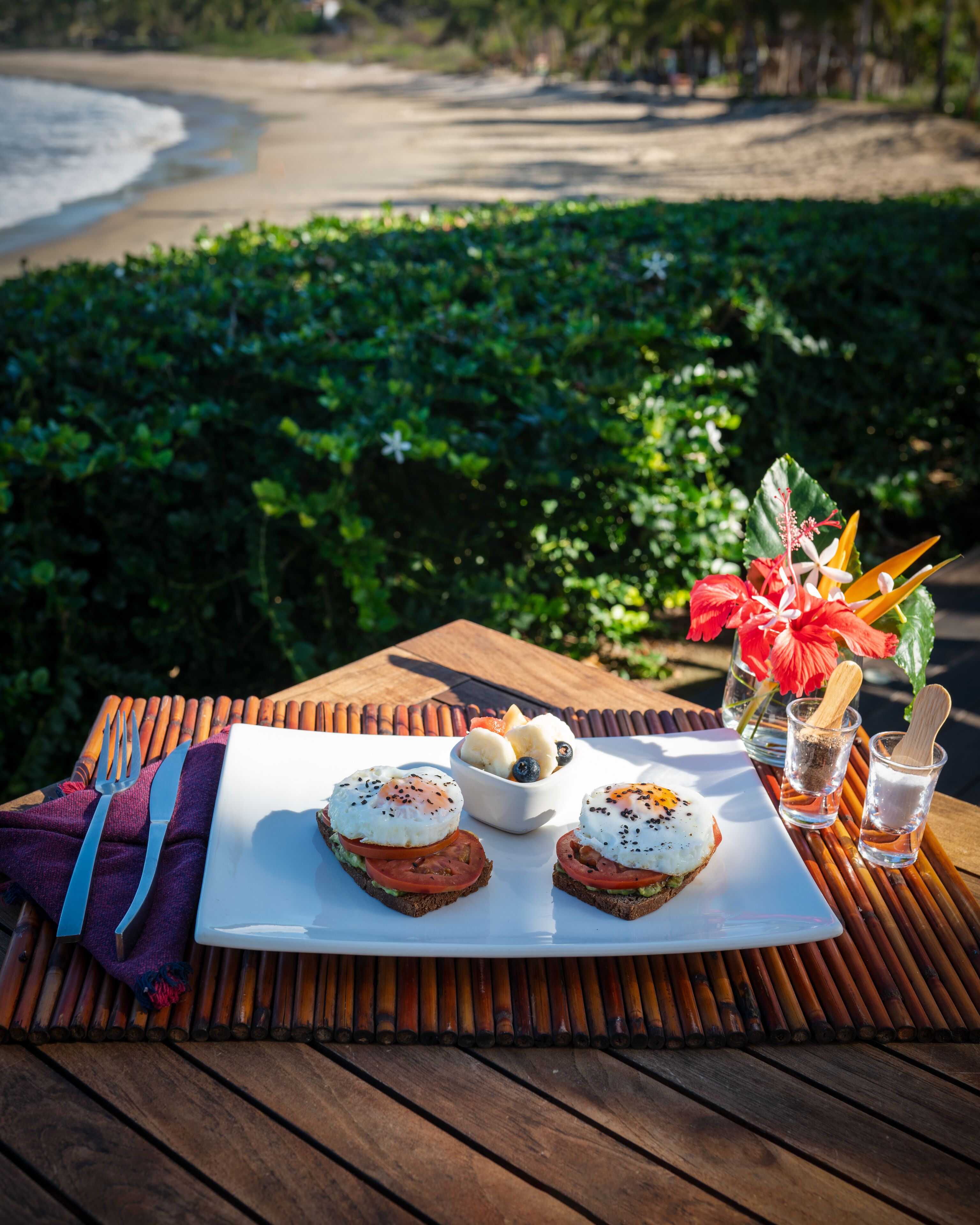 A table with breakfast items, a beach view, and a decorative flower arrangement.