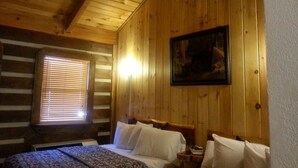 A wooden cabin room with a bed, a nightstand, and a painting on the wall. - Black Bear Lodge Motel (Slade)