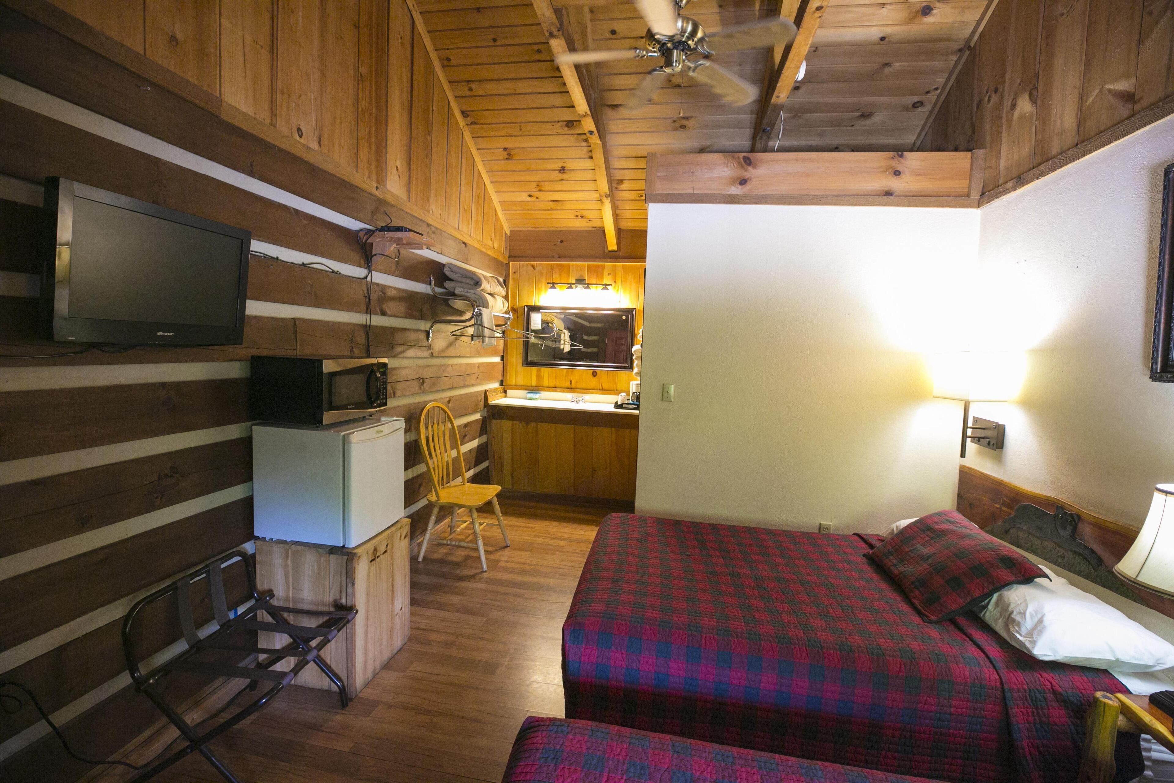 Una habitación acogedora tipo cabaña con una cama, un escritorio con computadora, una silla y un televisor.