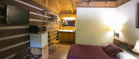 A cozy cabin room with a bed, a desk with a computer, a chair, and a television.