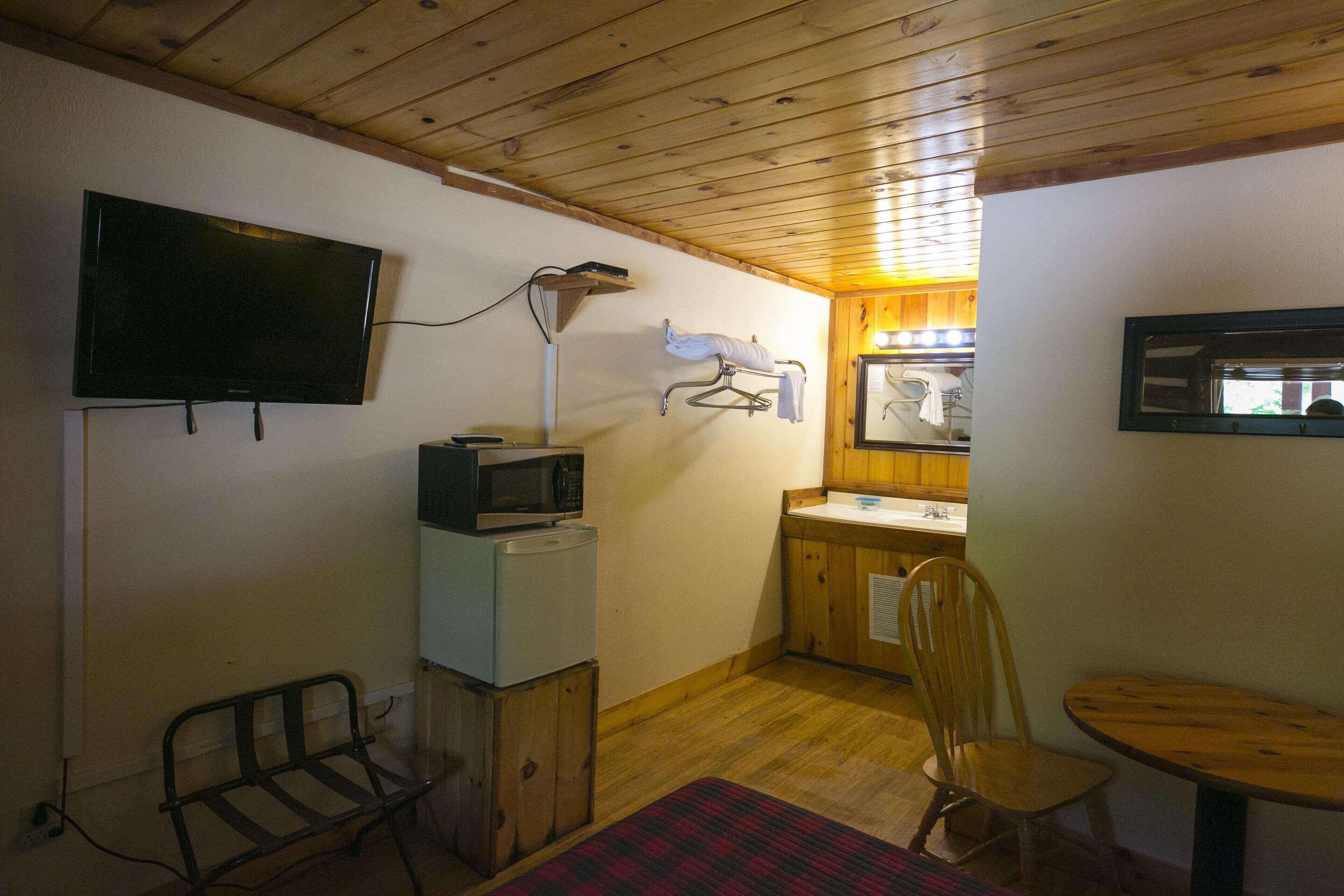 Habitació senzilla amb televisió, microones, nevera, sostre de fusta, taula de fusta i una cadira.