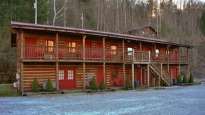 A two-story log cabin with a balcony, a covered porch, and a gravel driveway. - Black Bear Lodge Motel (Slade)