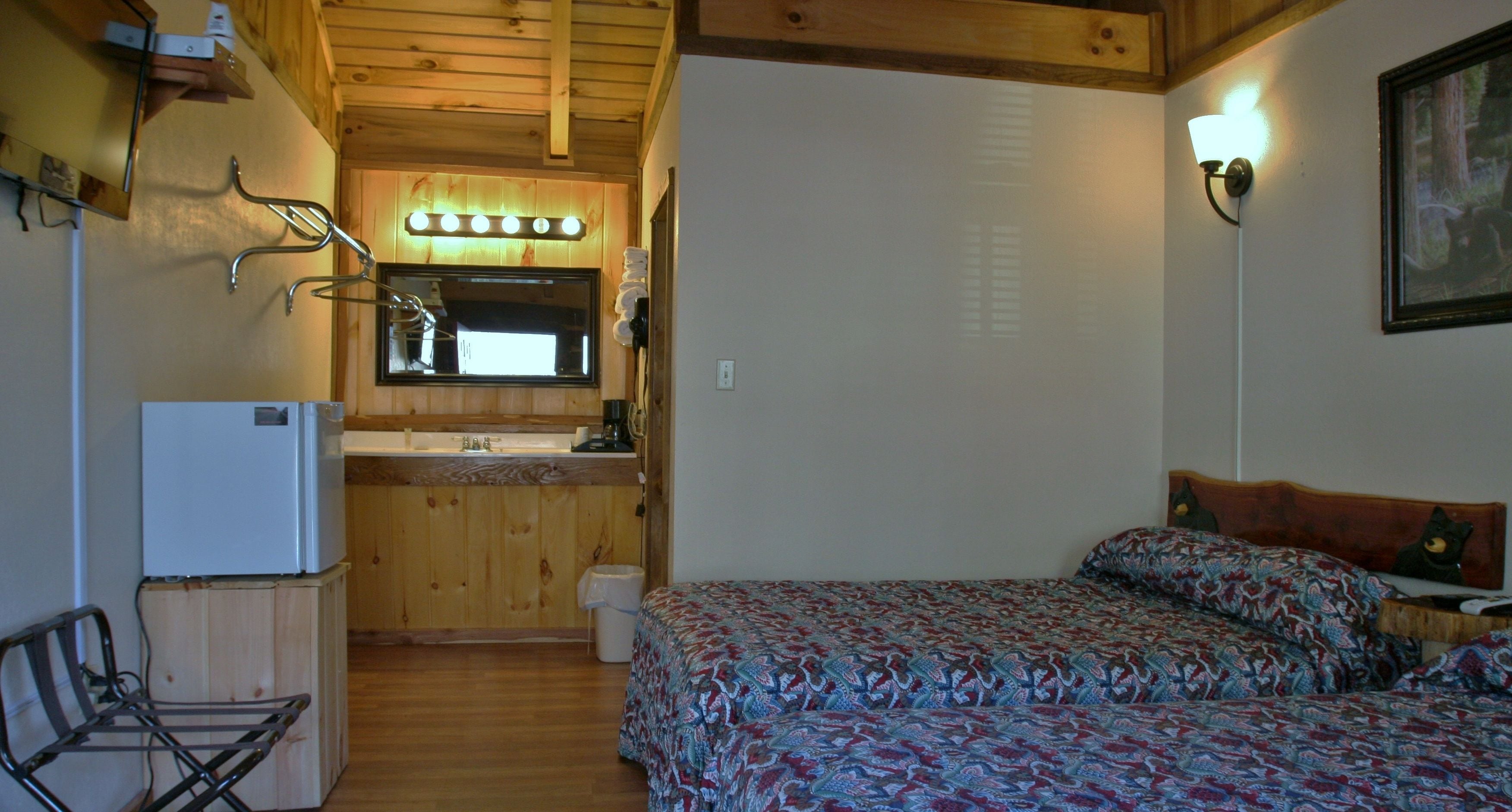 Una habitación compacta con cama, un pequeño rincón de cocina, un espejo y techo de madera.