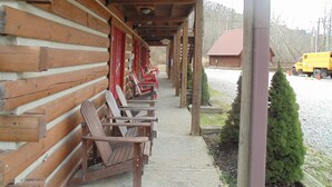 A log cabin with a covered porch and several wooden chairs. - Black Bear Lodge Motel (Slade)