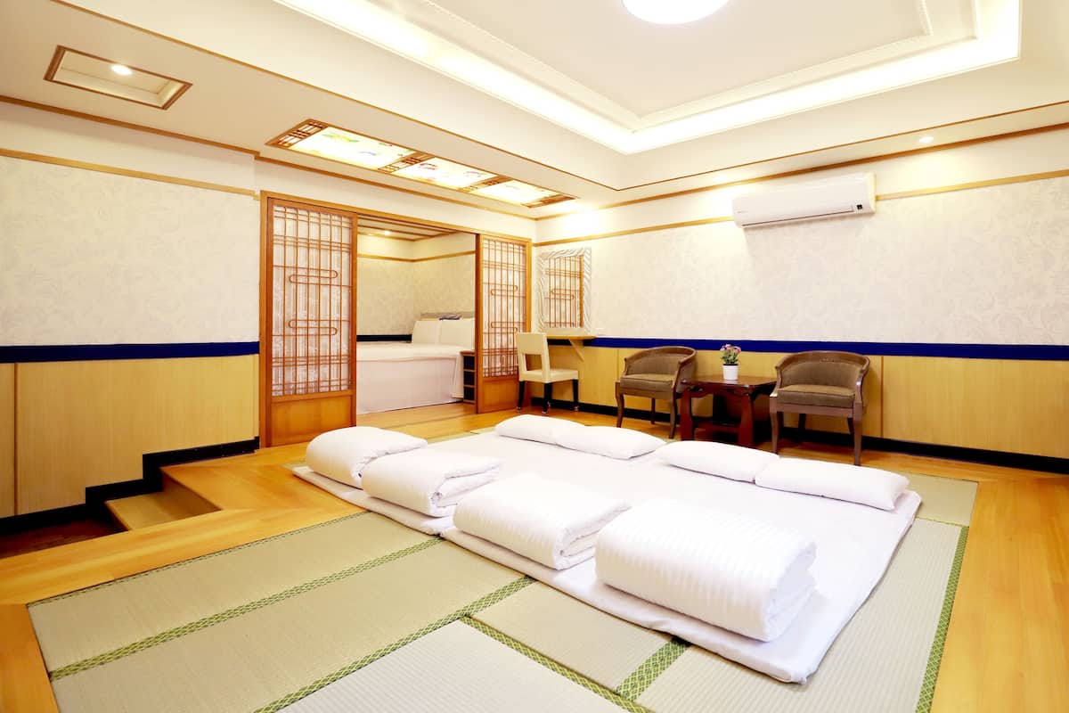 A traditional Japanese-style room with tatami flooring, a futon bed, a sliding door, a small table with a chair, and an air conditioning unit on the wall.