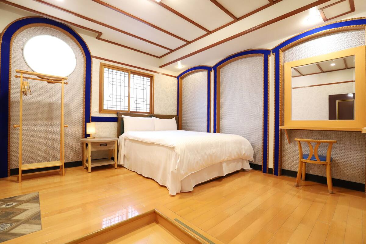 A bedroom with a bed, a nightstand, a chair, a mirror, and a window with a view.